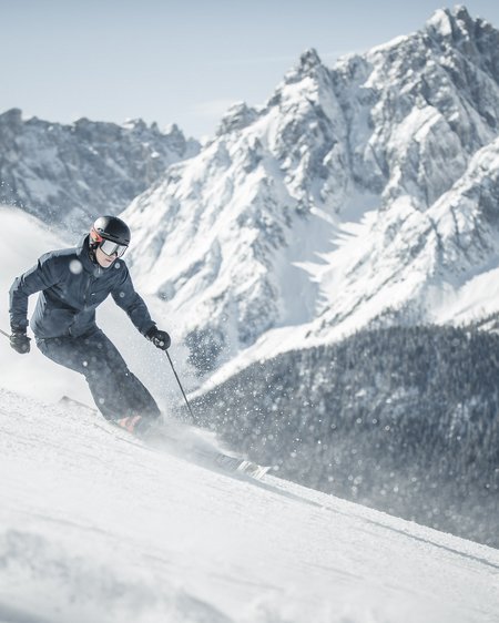 Our 5-star hotel in Italy between heaven and earth Skier skiing on snowy slope with large mountains in the background