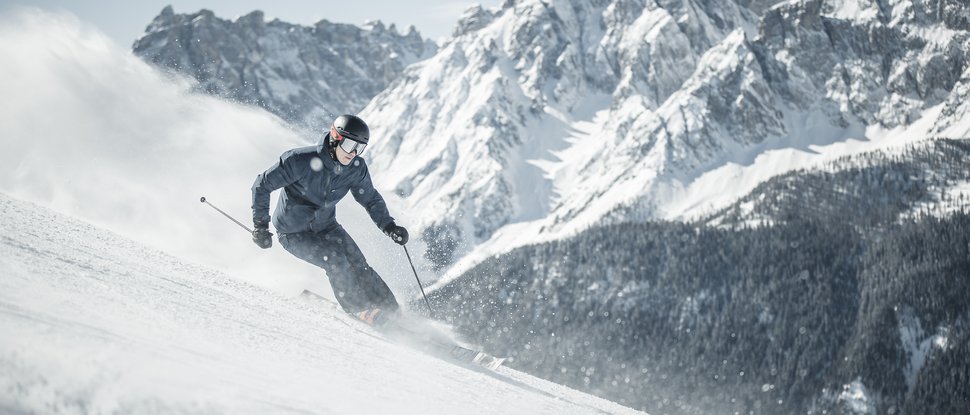 Unser Hotel in Olang zwischen Himmel und Erde Skifahrer fährt einen schneebedeckten Berg mit schroffen Gipfeln im Hintergrund hinab