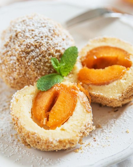 Unser Hotel in Olang zwischen Himmel und Erde Marillenknödel mit Zucker und Minzblatt auf weißem Teller