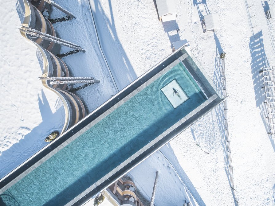 Unser Hotel in Olang zwischen Himmel und Erde Überblick auf ein beheiztes Außenbecken in einer verschneiten Winterlandschaft