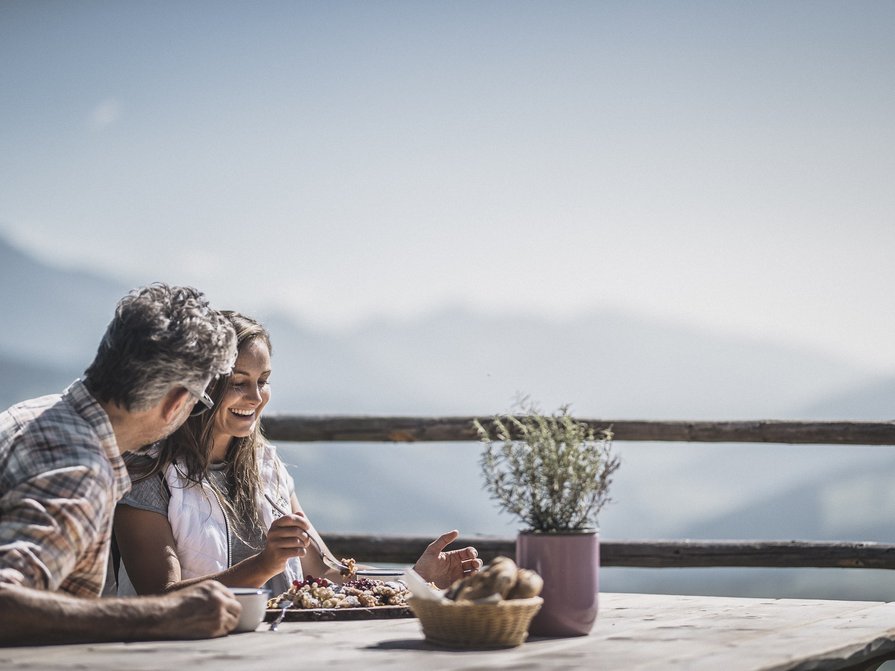 Unser Hotel in Olang zwischen Himmel und Erde Zwei Personen essen und unterhalten sich draußen mit Bergblick