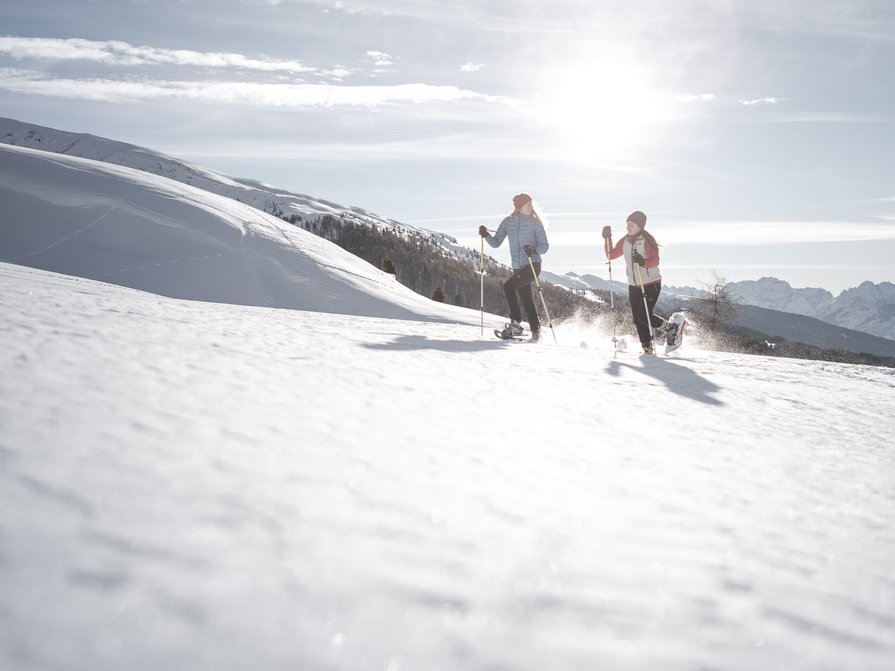 Unser Hotel in Olang zwischen Himmel und Erde Zwei Personen laufen mit Schneeschuhen im sonnigen Schnee in den Bergen