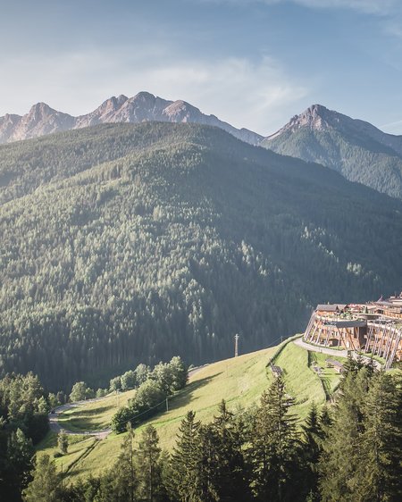 Unser Hotel in Olang zwischen Himmel und Erde Berglandschaft mit Wäldern und Gebäuden am Hang unter klarem Himmel
