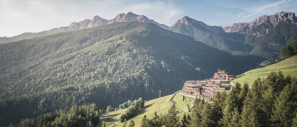 Unser Hotel in Olang zwischen Himmel und Erde Berglandschaft mit Wäldern und Gebäuden am Hang unter klarem Himmel