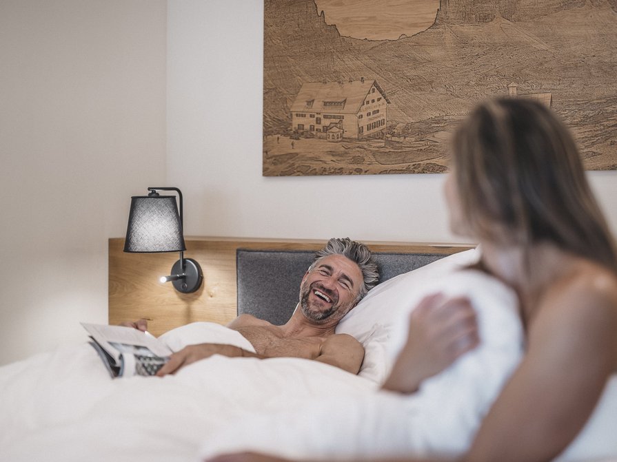 Unser Hotel in Olang zwischen Himmel und Erde Mann und Frau lachen gemeinsam im Bett unter weißer Bettdecke