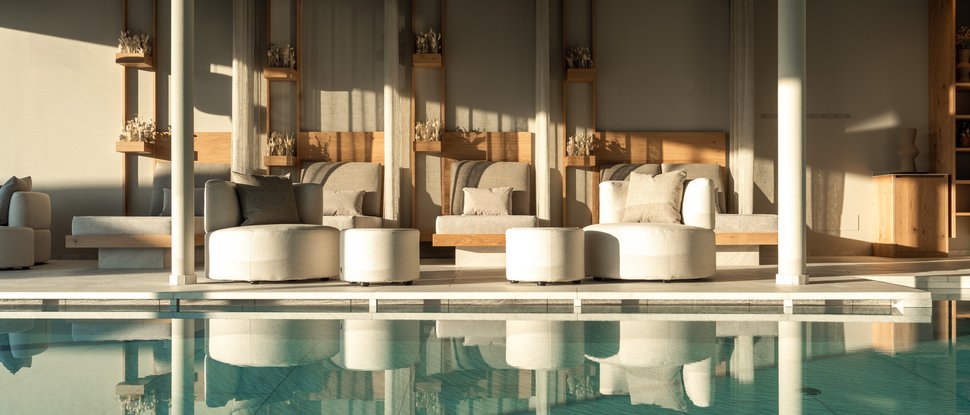 Unser Hotel in Olang zwischen Himmel und Erde Gemütliche Sitzplätze neben einem stillen Innenpool mit Sonnenlicht