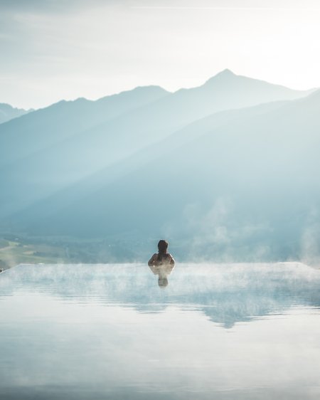 Unser Hotel in Olang zwischen Himmel und Erde Person in dampfendem Infinity-Pool mit Blick auf neblige Berglandschaft