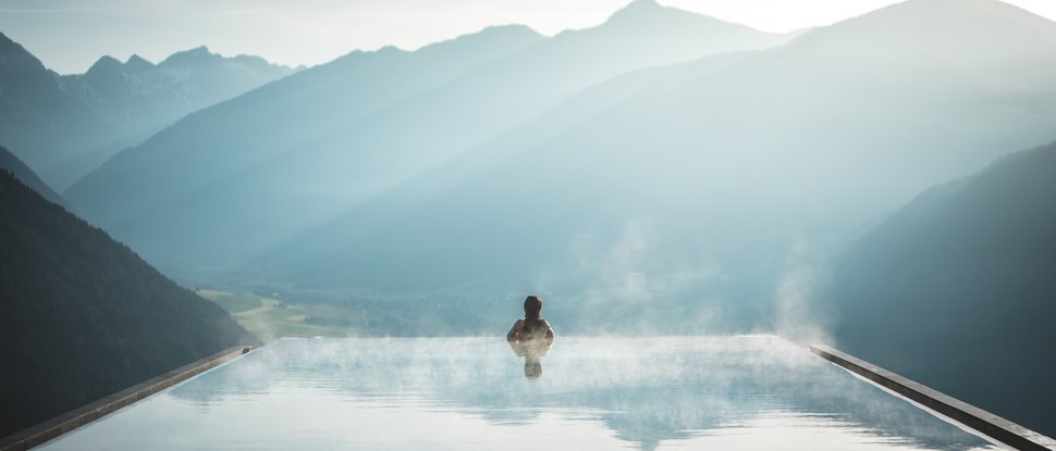 Unser Hotel in Olang zwischen Himmel und Erde Person in dampfendem Infinity-Pool mit Blick auf neblige Berglandschaft