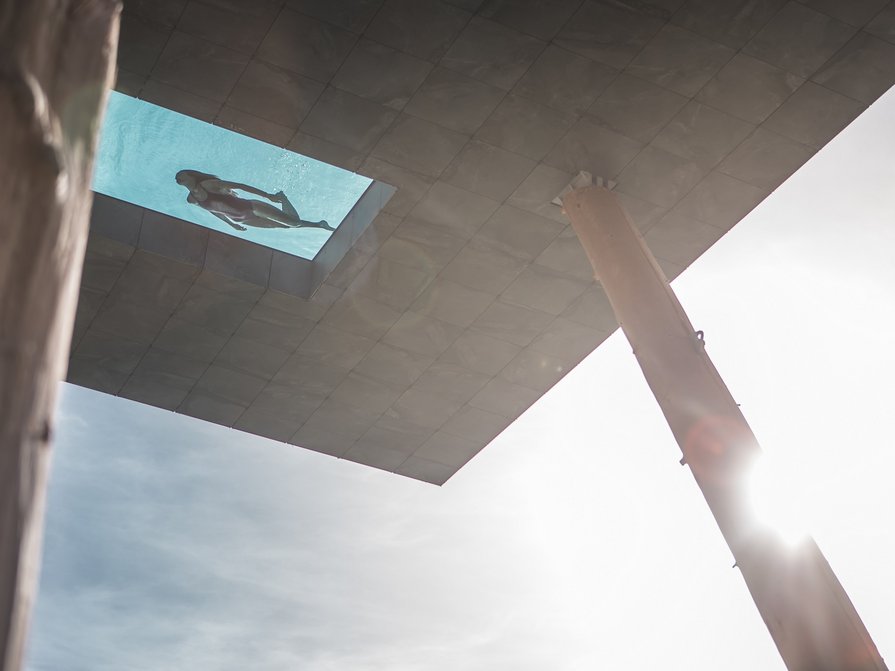 Unser Hotel in Olang zwischen Himmel und Erde Frau schwimmt in einem Pool mit Glasboden über einem Gebäude