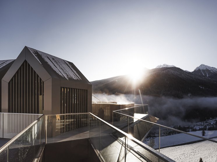 Heaven & hell, our new highlight Modern rooftop terrace with glass railing and sun over snowy mountains