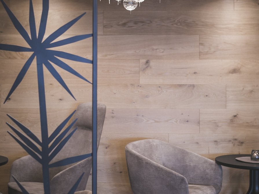 Unser Hotel in Olang zwischen Himmel und Erde Gemütliche Sitzecke mit grauem Sessel und rundem Tisch vor Holzwand