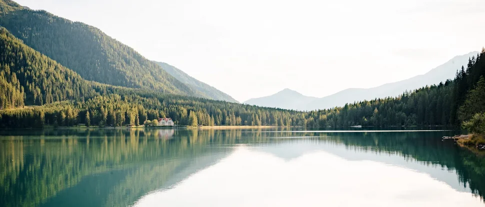 Unser Hotel in Olang zwischen Himmel und Erde Bergsee mit reflektierenden Bäumen und einem Haus am Ufer