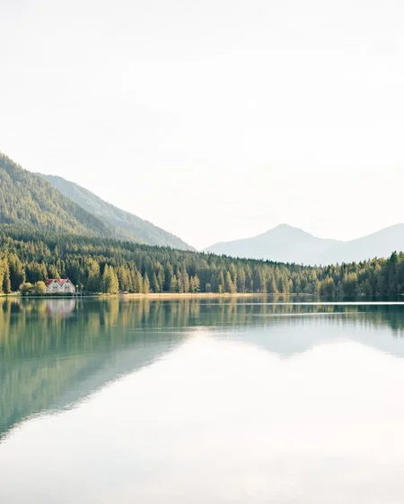 Unser Hotel in Olang zwischen Himmel und Erde Bergsee mit reflektierenden Bäumen und einem Haus am Ufer